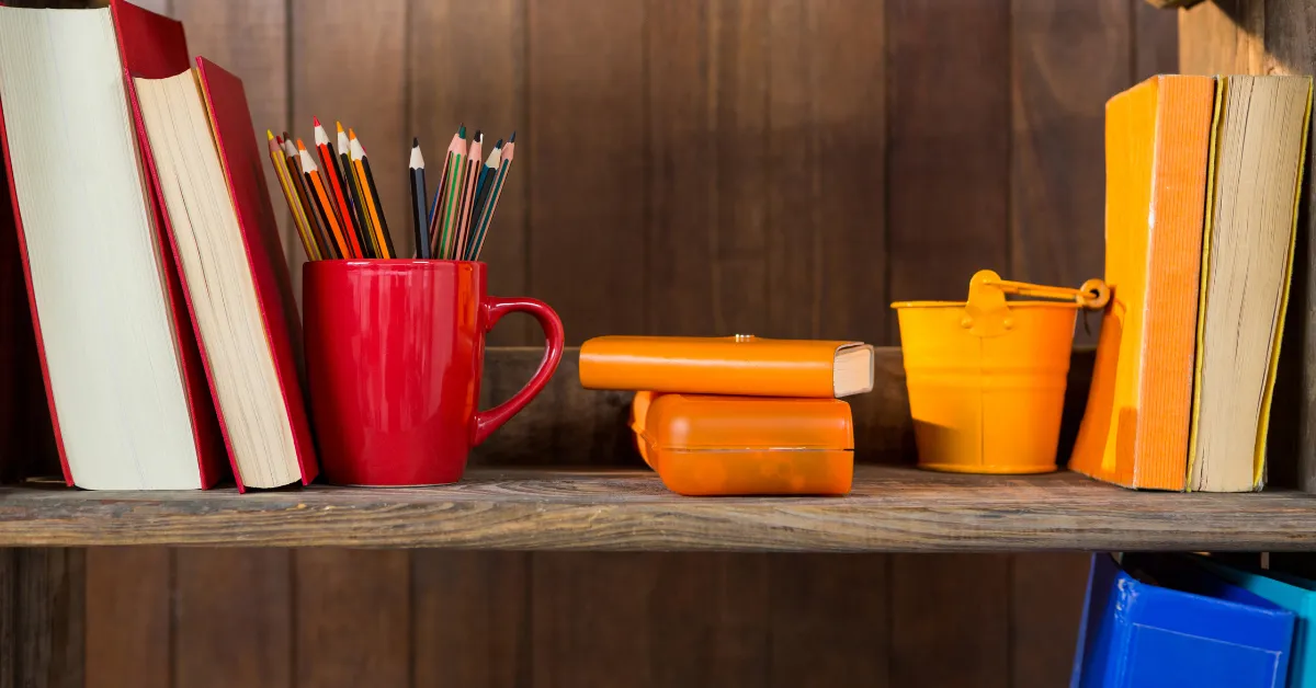 Elf on the shelf ideas for a classroom with books, pencils in red mug and colorful supplies shelf.
